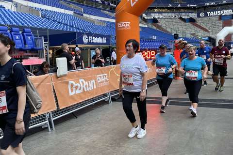 Mehrere Personen gehen unter einem orangefarbenen Zielbogen mit der Aufschrift „B2Run“ in einem Stadion.