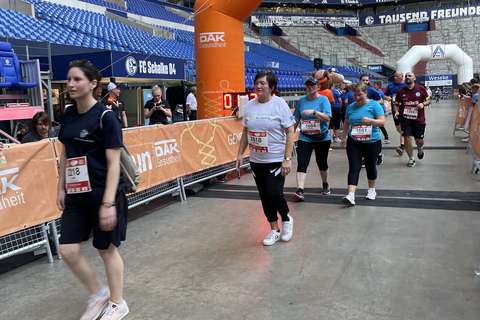 Mehrere Personen gehen durch einen orangefarbenen Zielbogen in einem Stadion.