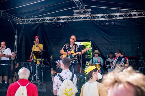 Mehrere Personen musizieren auf einer Bühne, während einige Personen davor stehen und zuhören.