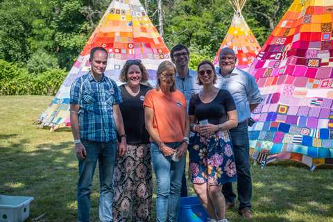 Sechs Personen stehen auf einer Wiese vor drei bunten Tipis aus Patchwork.