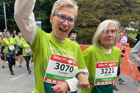 Zwei Personen mit Startnummern und grünen Laufshirts gehen nebeneinander bei einer Laufveranstaltung.