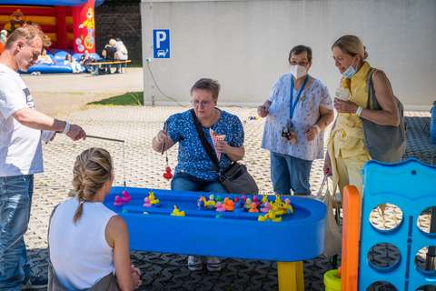Fünf Personen spielen an einem blauen Wasserbecken mit bunten Plastikenten und Angeln.