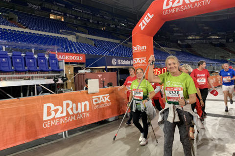 Mehrere Personen überqueren mit Startnummern und Sportkleidung die Ziellinie eines Lauf-Events in einem Stadion.
