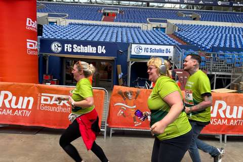 Drei Personen in grünen T-Shirts laufen nebeneinander in einem Stadion.