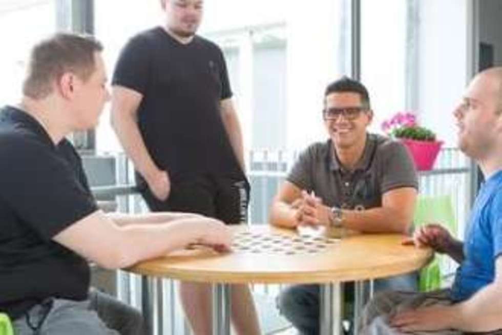 Vier Personen befinden sich an einem runden Tisch, eine Person sitzt im Rollstuhl.