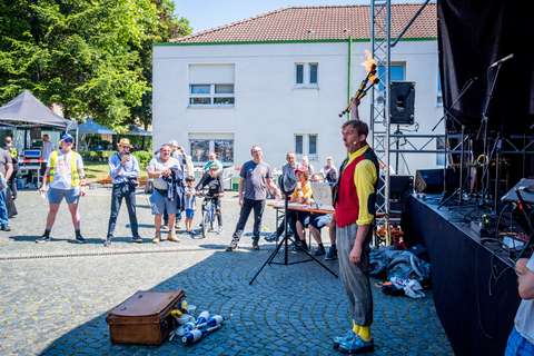 Eine Person in bunter Kleidung hält brennende Fackeln in der Hand, während mehrere Personen im Freien zuschauen.
