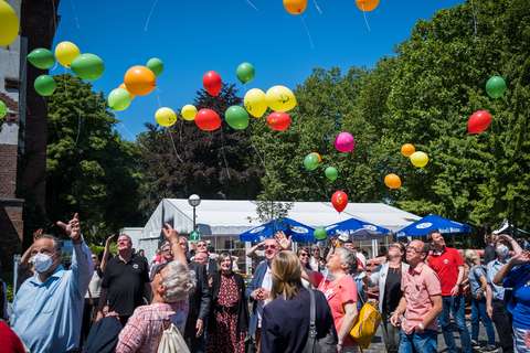 Mehrere Personen stehen im Freien und schauen bunten Luftballons nach, die in den Himmel steigen.
