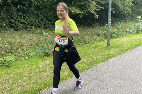Eine Person mit Startnummer 3210 geht auf einer asphaltierten Straße neben einer Wiese und trägt Sportkleidung.
