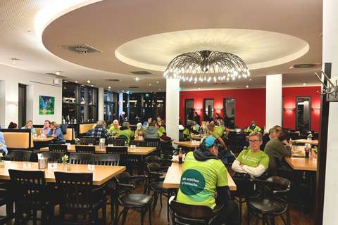 Mehrere Personen sitzen an Tischen in einem hell beleuchteten Restaurant.