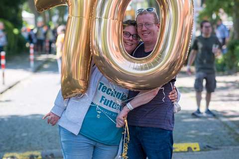 Zwei Personen stehen auf einer Straße und halten goldene Luftballons in Form der Zahl 10.
