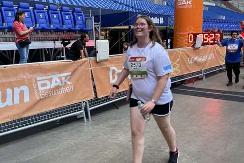 Eine Person mit Startnummer läuft in Sportkleidung an einer Ziellinie in einem Stadion vorbei.