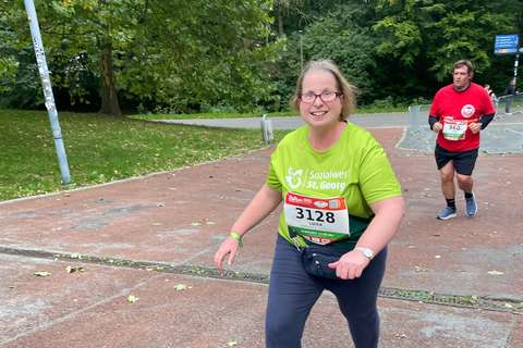 Zwei Personen laufen auf einer asphaltierten Strecke im Freien, eine trägt ein grünes T-Shirt und die andere ein rotes T-Shirt.
