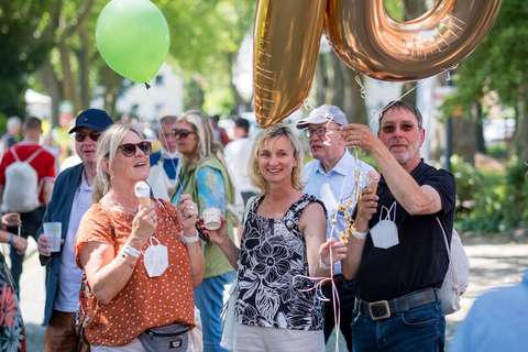 Drei Personen stehen im Freien, halten Luftballons in Form der Zahl 70 und einen grünen Ballon.
