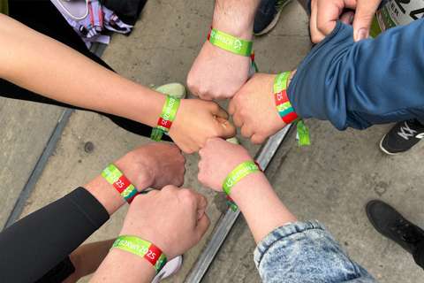 Sieben Personen halten ihre Fäuste zusammen, alle tragen grüne Armbänder mit der Aufschrift „B2Run 2025“.