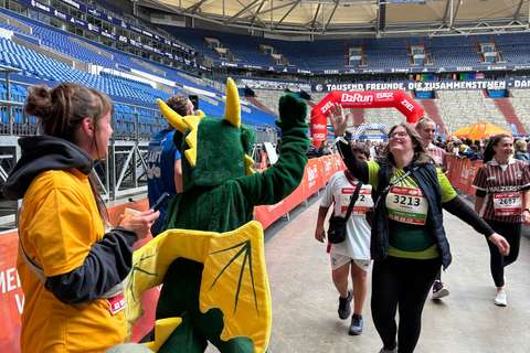 Mehrere Personen, darunter eine Person im Drachenkostüm, geben sich bei einer Laufveranstaltung in einem Stadion ein High-Five.