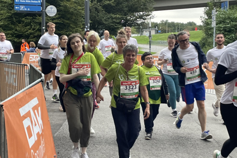 Mehrere Personen nehmen an einem Laufwettbewerb teil und tragen Startnummern sowie Sportkleidung, einige in grünen T-Shirts, andere in weißen.