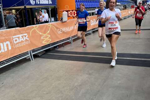 Mehrere Personen laufen unter einem orangefarbenen Zielbogen in einem Stadion.