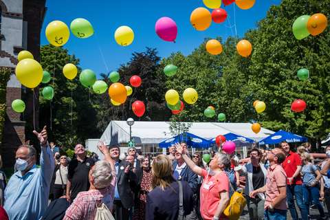 Mehrere Personen stehen im Freien und lassen bunte Luftballons in den Himmel steigen.