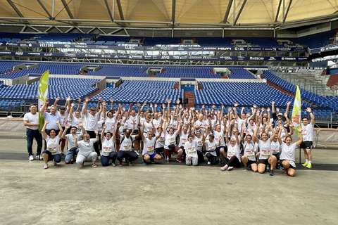 Eine große Gruppe von Personen in weißen T-Shirts steht und kniet in einem Stadion, viele heben die Arme hoch.