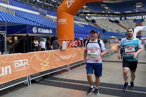 Zwei Personen überqueren eine Ziellinie unter einem orangefarbenen Torbogen in einem Stadion.