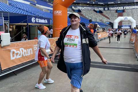 Eine Person mit Startnummer überquert die Ziellinie bei einer Laufveranstaltung in einem Stadion.