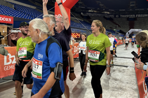 Mehrere Personen überqueren eine Ziellinie bei einer Laufveranstaltung in einem Stadion.