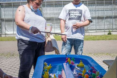 Zwei Personen stehen an einem blauen Wasserbecken mit bunten Plastikenten und Angeln.