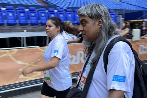 Zwei Personen in Sportkleidung gehen nebeneinander in einem Stadion mit blauen Sitzreihen.