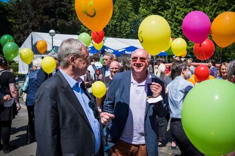 Mehrere Personen stehen im Freien zwischen bunten Luftballons.