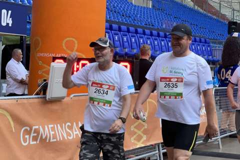 Zwei Personen mit Startnummern und Sportkleidung gehen nebeneinander durch einen Zieleinlauf in einem Stadion.