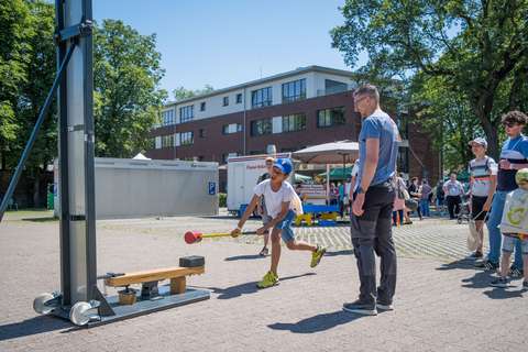 Eine Person schlägt mit einem Hammer auf ein Jahrmarkts-Spielgerät, während mehrere Personen zuschauen.
