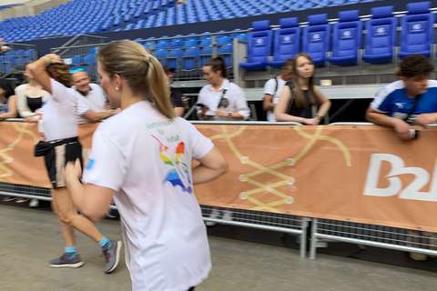 Eine Person läuft in einem Stadion an einer Absperrung vorbei, im Hintergrund sitzen und stehen mehrere Personen vor leeren blauen Sitzreihen.