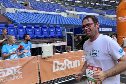 Eine Person läuft in einem Stadion an einer Absperrung mit B2Run-Banner vorbei, im Hintergrund sitzen und stehen weitere Personen.