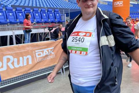 Eine Person mit Startnummer 2540 und Kappe geht in einem Stadion an einem Zielbogen vorbei.