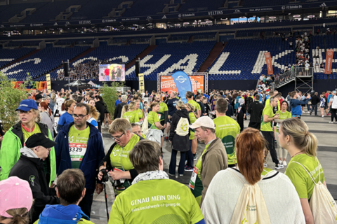 Viele Personen stehen in einer großen Halle mit Tribünen, viele tragen grüne T-Shirts und Startnummern.