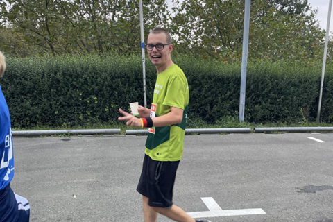 Eine Person in Sportkleidung geht auf einer Straße und hält einen Becher in der Hand.