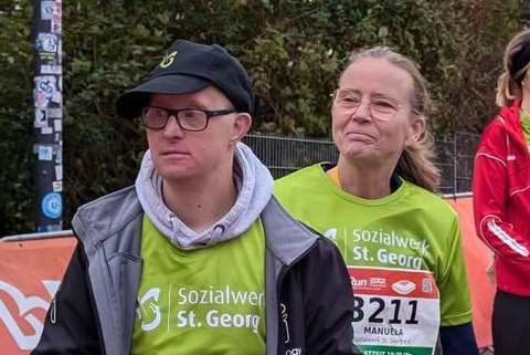 Zwei Personen in Sportkleidung mit Startnummern und Nordic-Walking-Stöcken stehen nebeneinander auf einer Laufstrecke.