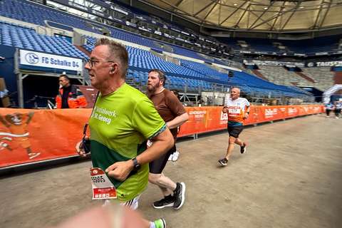 Drei Personen laufen in einem Stadion auf einer abgesperrten Strecke.