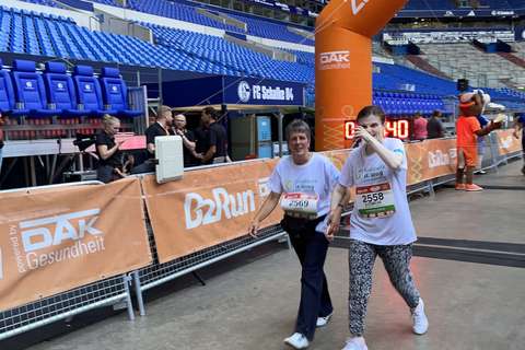 Zwei Personen gehen Hand in Hand durch einen Zielbogen bei einer Laufveranstaltung in einem Stadion.