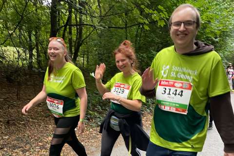 Drei Personen mit Startnummern und grünen T-Shirts gehen auf einem Waldweg.
