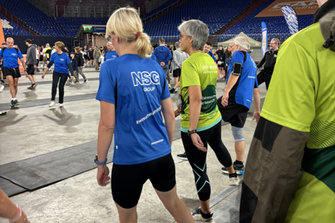 Mehrere Personen in Sportkleidung gehen in einer großen Halle mit Tribünen.