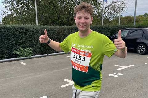 Eine Person mit Startnummer läuft auf einer Straße und zeigt beide Daumen nach oben.