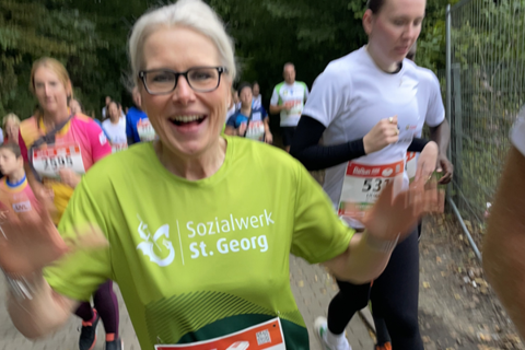 Mehrere Personen laufen auf einem Weg, eine Person im Vordergrund trägt ein grünes Laufshirt und eine Startnummer.