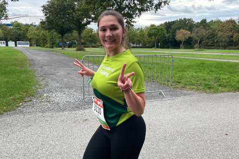 Eine Person mit Startnummer läuft auf einem Weg im Freien und zeigt mit beiden Händen das Peace-Zeichen.