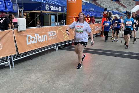 Eine Person mit Startnummer überquert die Ziellinie bei einer Laufveranstaltung in einem Stadion.
