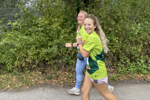 Zwei Personen joggen auf einem Weg neben grüner Vegetation.