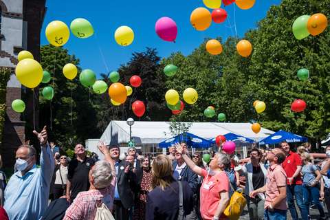 Mehrere Personen stehen im Freien und lassen bunte Luftballons steigen.