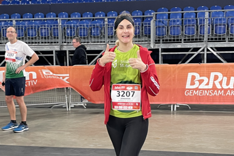 Eine Person mit Startnummer läuft in Sportkleidung in einer Halle und zeigt beide Daumen nach oben.