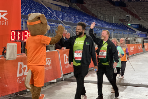 Eine Person im Tierkostüm gibt mehreren Personen, die Laufnummern tragen, ein High-Five.