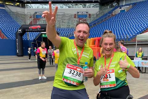 Zwei Personen mit Startnummern und Medaillen tragen grüne Laufshirts in einem Stadion.